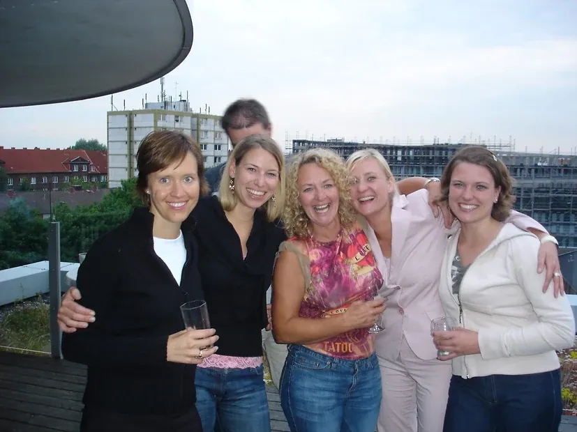 Sechs Personen mit Gläsern auf einer Dachterrasse, dahinter Wohnhäuser und ein Baukran