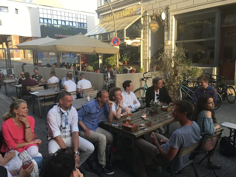 Eine Gruppe sitzt abends an Biertischen vor einem Lokal mit der Aufschrift „Schlachterbörse“