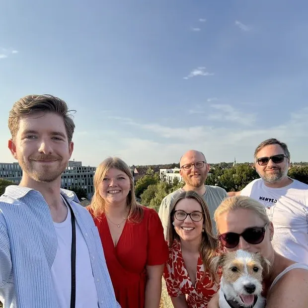 Selfie von sechs Personen mit einem kleinen Hund auf einer Dachterrasse im Abendlicht