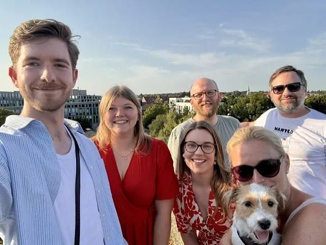Selfie von sechs Personen mit einem kleinen Hund auf einer Dachterrasse im Abendlicht