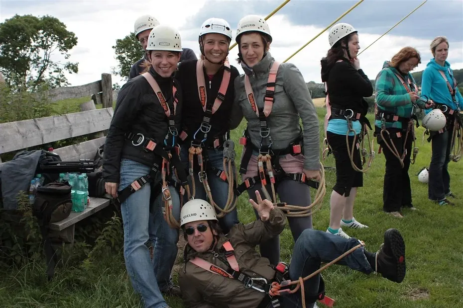 Eine Gruppe in Klettergurten und Helmen steht auf einer Wiese, daneben gespannte Seile