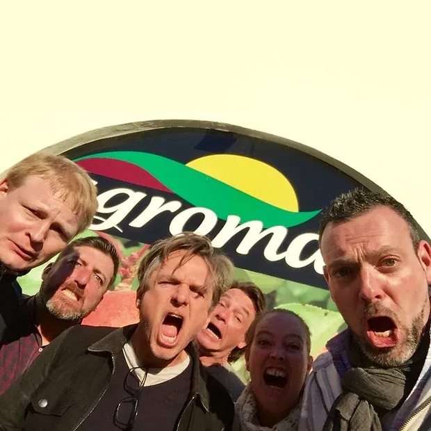Sechs Personen schneiden im Selfie Grimassen vor einem großen runden Werbeschild