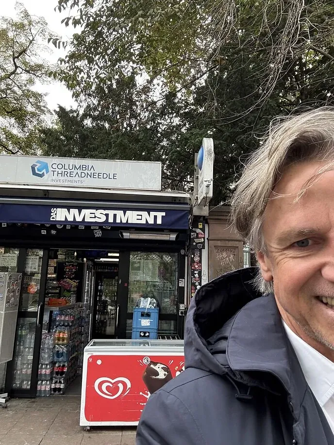 Selfie vor einem Kiosk, dessen Markise den Schriftzug „DAS INVESTMENT“ trägt