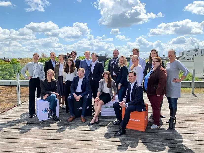 Das Team im Gruppenbild auf einer begrünten Dachterrasse vor blauem Himmel