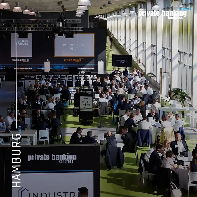 Blick von oben in eine helle Halle mit vielen runden Tischen; Leinwände und Banner weisen die Runde als „Round Tables“ des private banking kongress aus