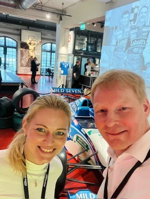 Selfie von zwei Personen vor einem ausgestellten Formel-1-Rennwagen in einer Halle