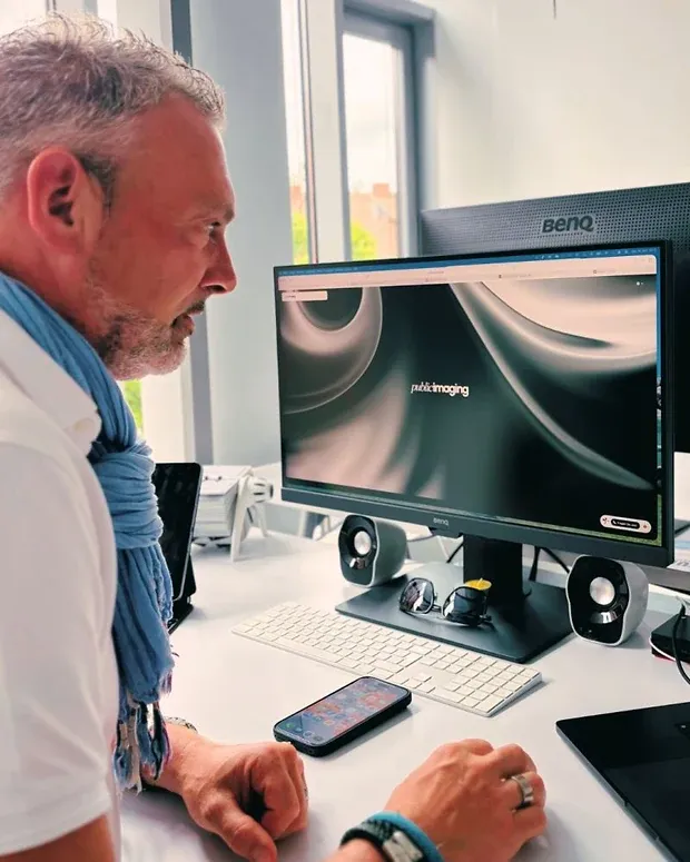 Ein Mann sitzt am Schreibtisch vor einem Monitor, auf dem die Startseite von public imaging geöffnet ist