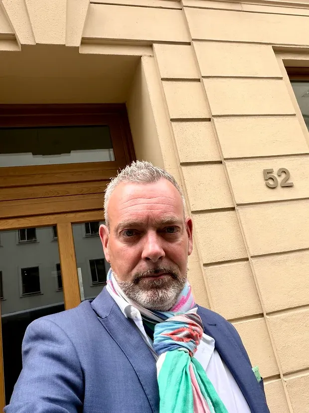 Selfie eines Mannes im blauen Sakko vor einem Altbauportal mit der Hausnummer 52