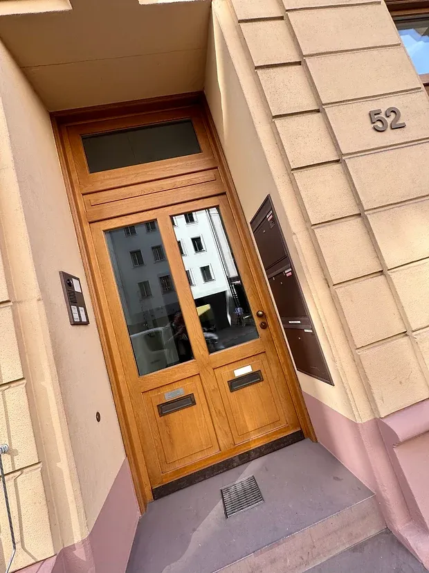 Zweiflügelige Haustür aus hellem Holz mit Briefkastenanlage, daneben die Hausnummer 52