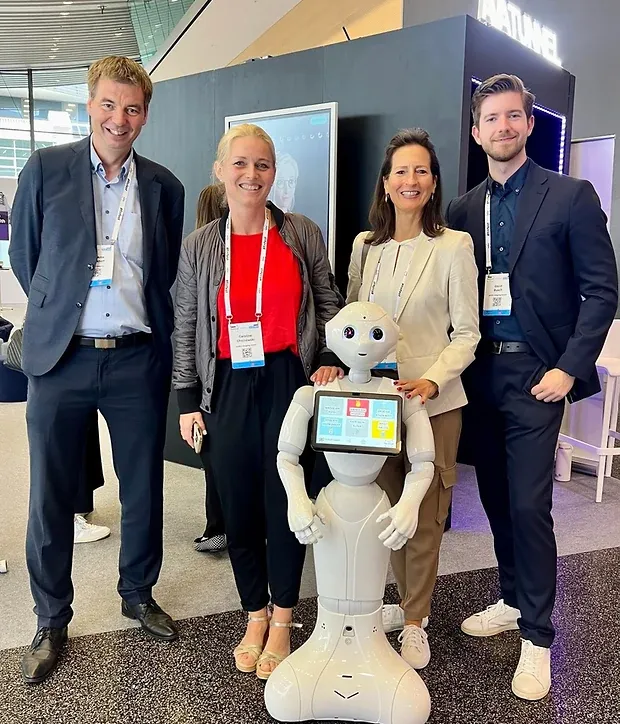 Vier Personen stehen um einen humanoiden Roboter mit Bildschirm auf der Brust