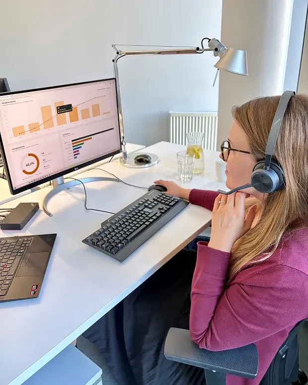 Eine Frau mit Headset sitzt am Schreibtisch vor einem Monitor mit einem Auswertungsbildschirm aus Balkendiagramm und Ringgrafik